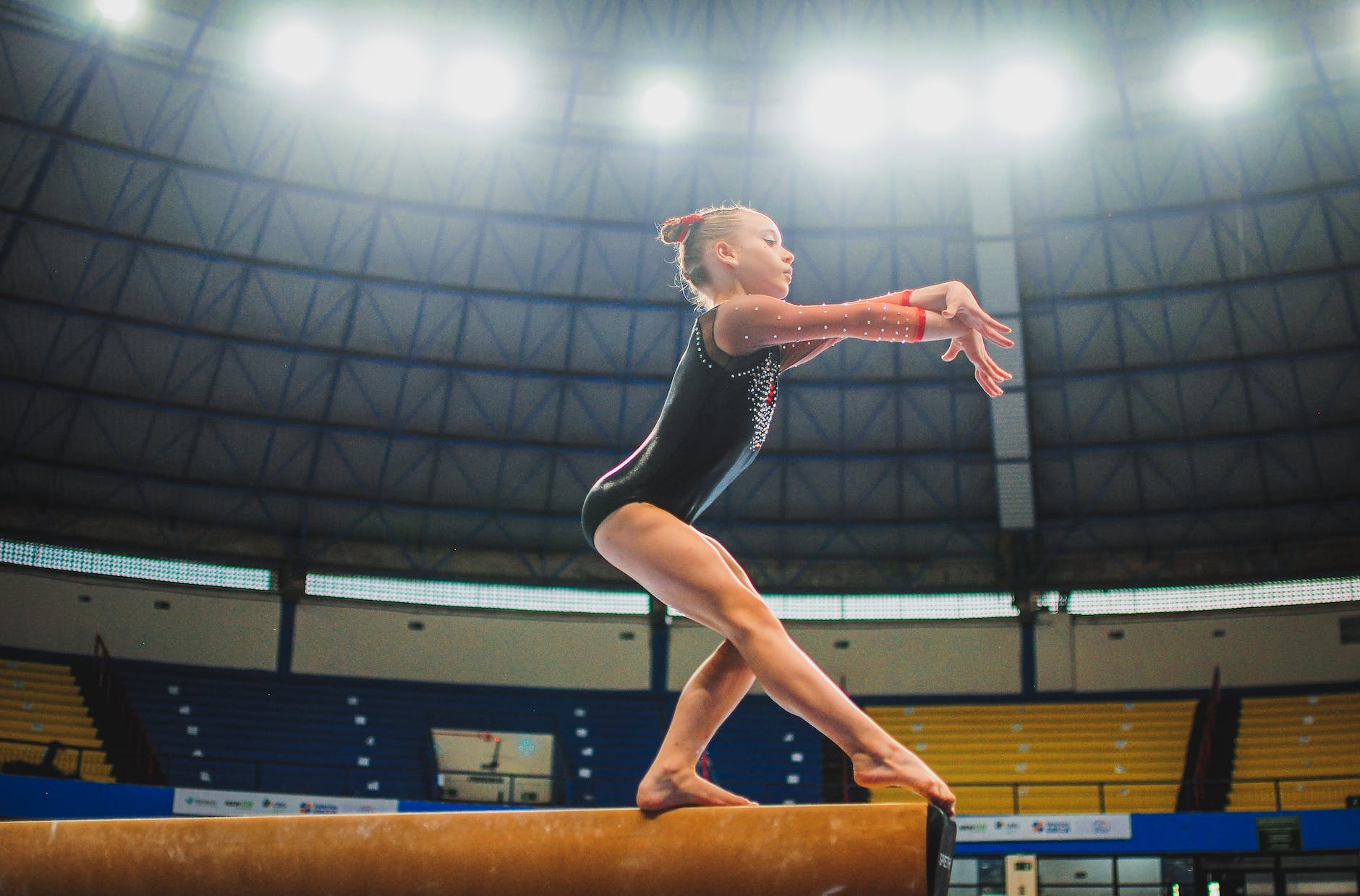 a girl in black leotards standing on balance beam