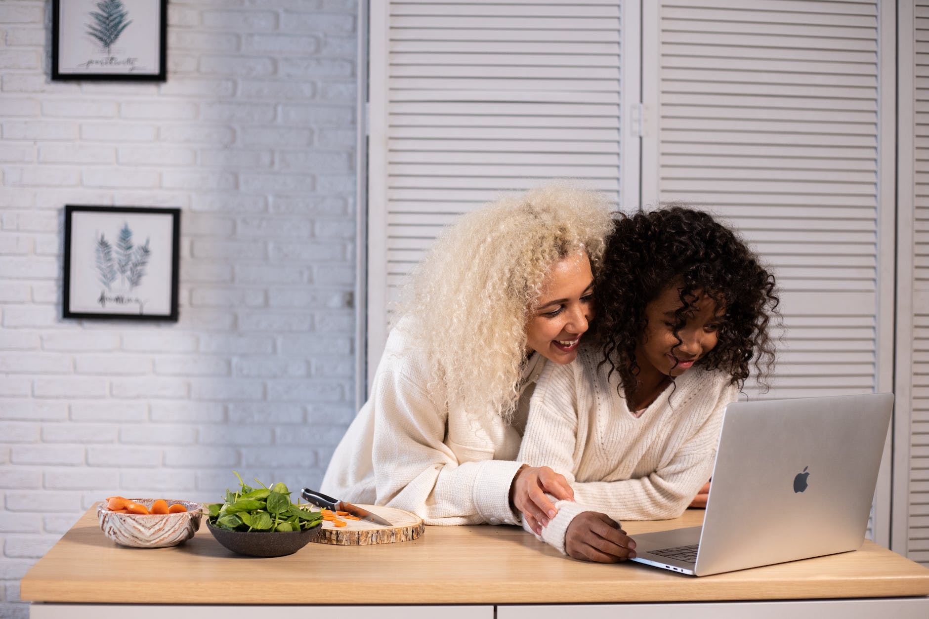 smiling black mother and daughter browsing laptop at kitchen counter
