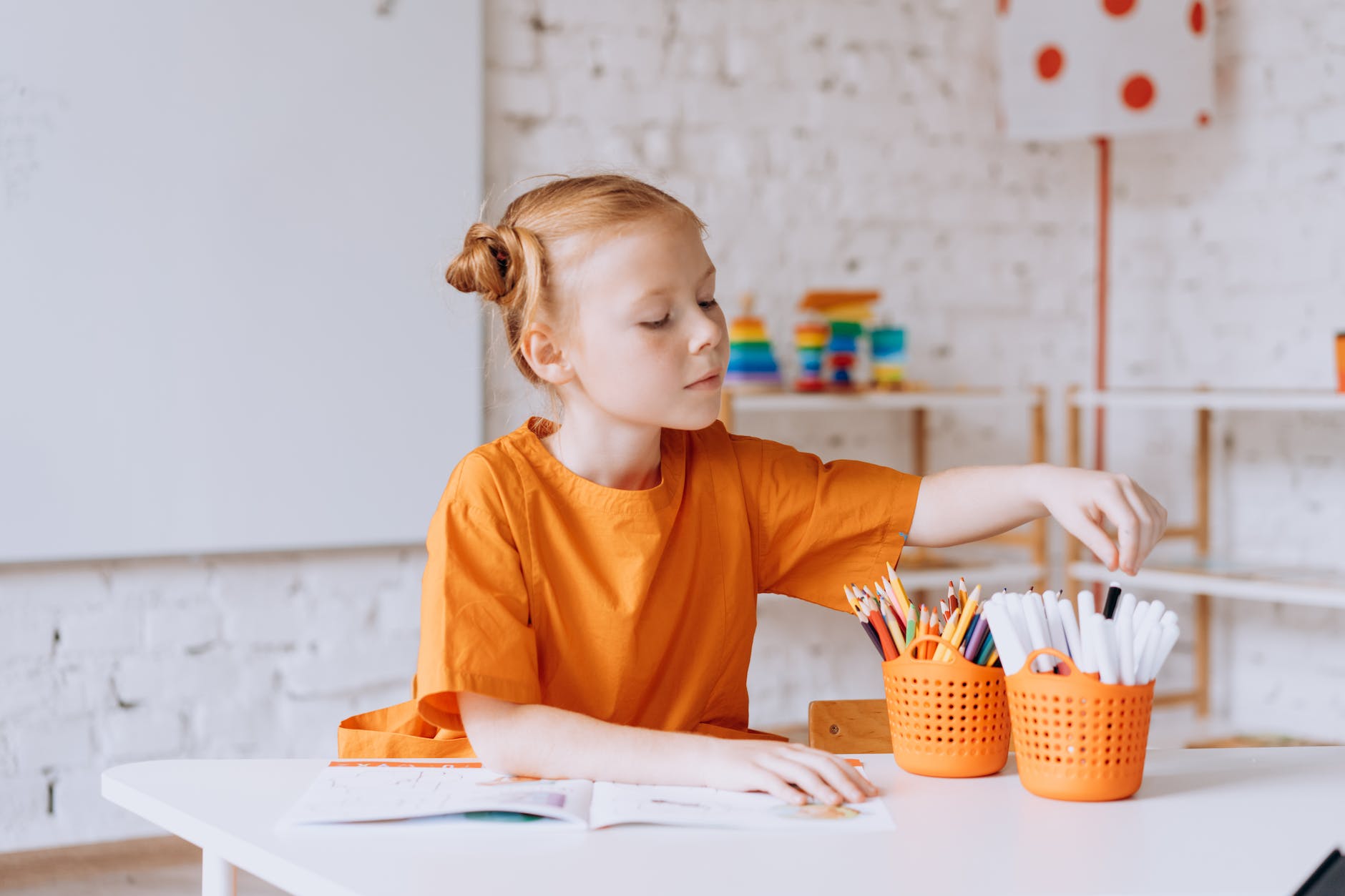 a girl in the classroom sitting at the desk with colored pencils