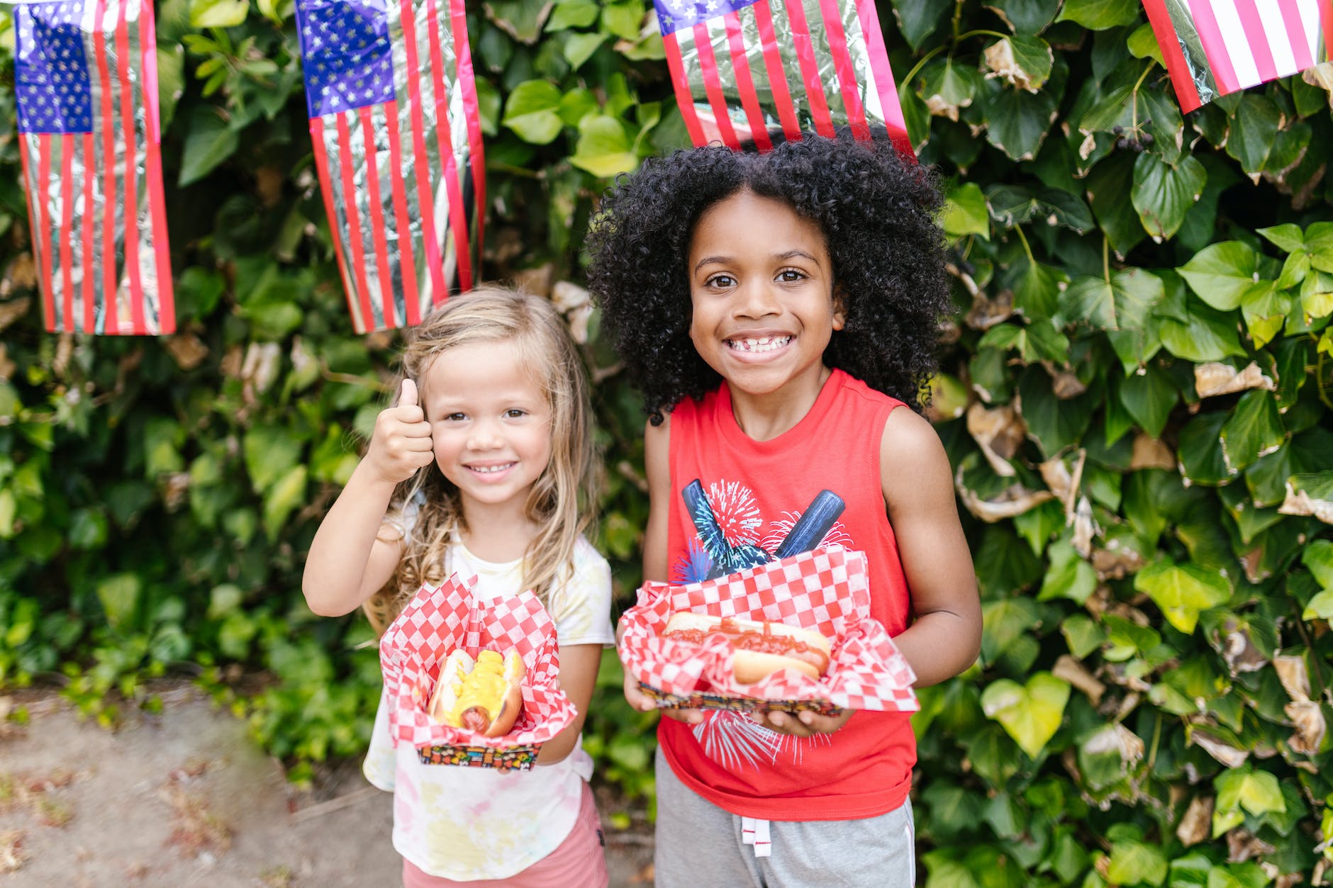 a young girl and boy smiling while holding hot dog sandwiches